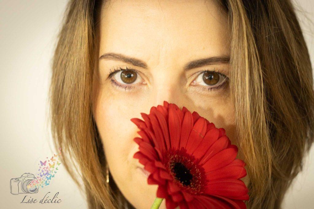 Portrait en gros plan d’une femme tenant une fleur rouge devant son visage – séance photo confiance en soi Lise Déclic