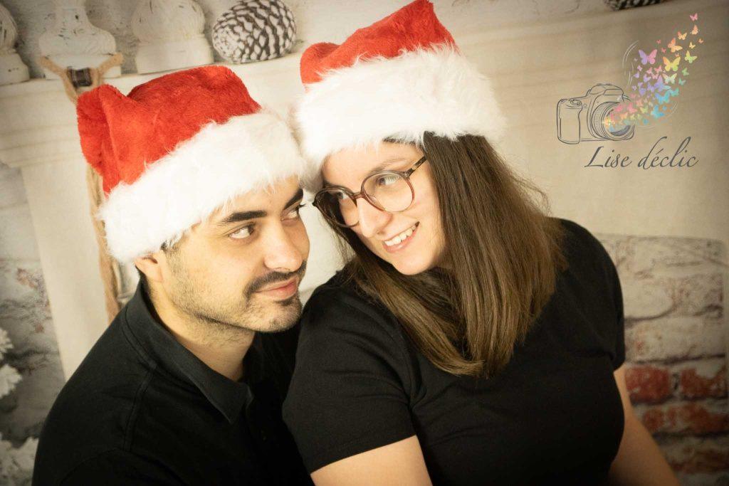 Couple portant des bonnets de Père Noël échangeant un regard complice lors d’une mini séance photo de Noël