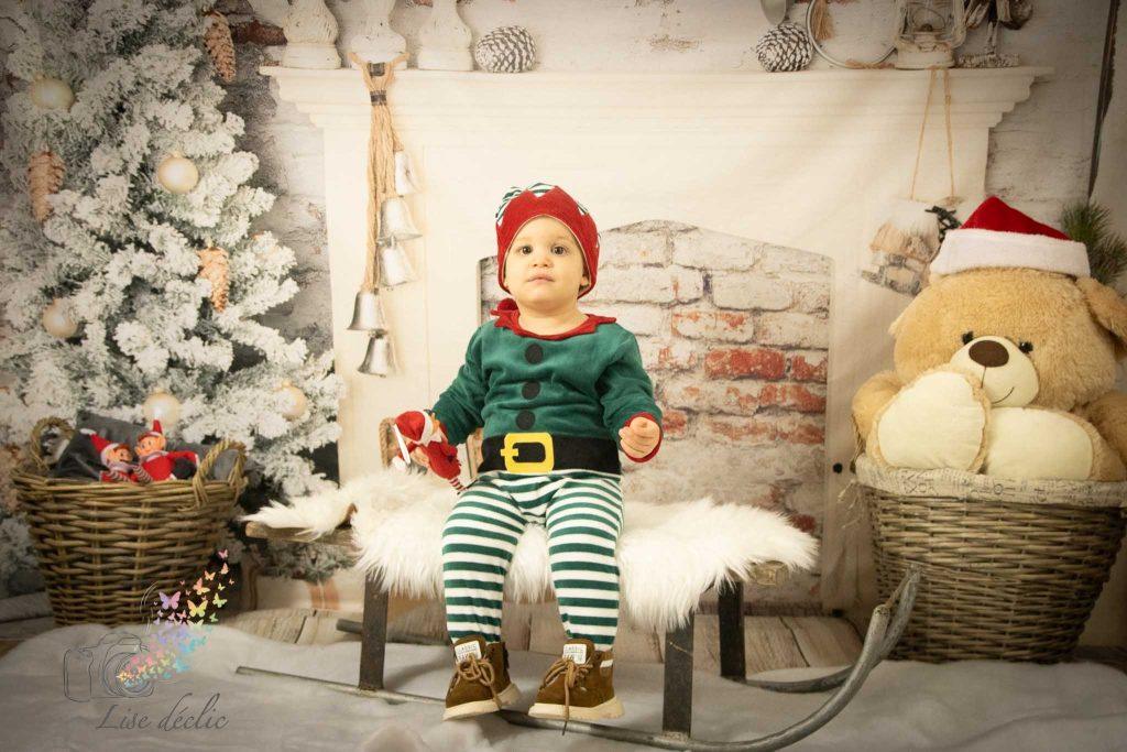 Enfant déguisé en lutin de Noël assis devant une cheminée décorée lors d’une mini séance photo de Noël