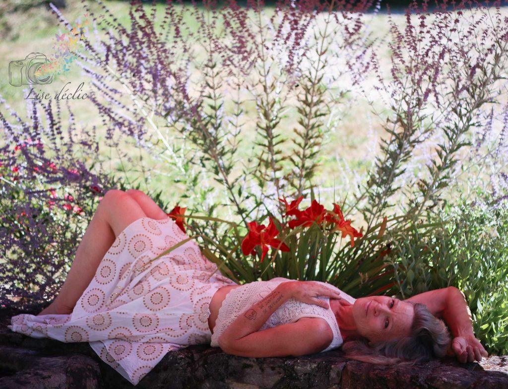 Portrait en extérieur d’une femme allongée dans un jardin fleuri – séance photo confiance en soi Lise Déclic