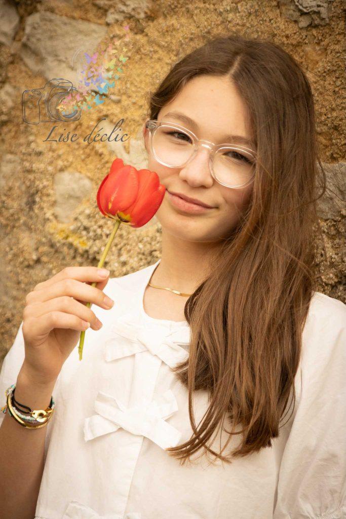 Jeune adolescente souriante tenant une tulipe rouge lors d’une séance photo authentique en extérieur