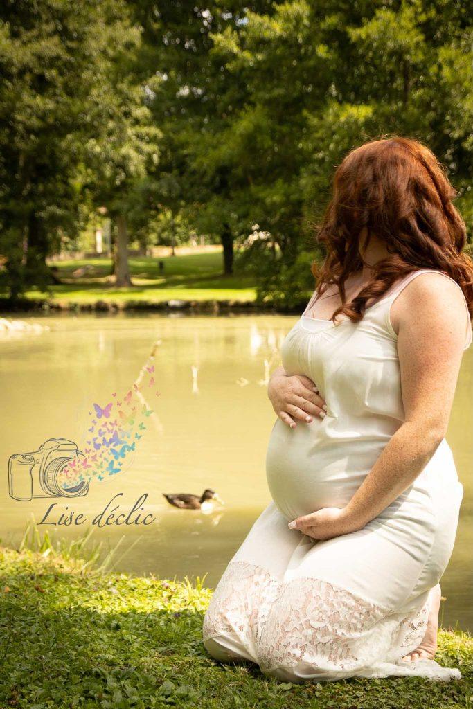 Femme enceinte agenouillée près d’un étang en pleine nature lors d’une séance photo grossesse authentique