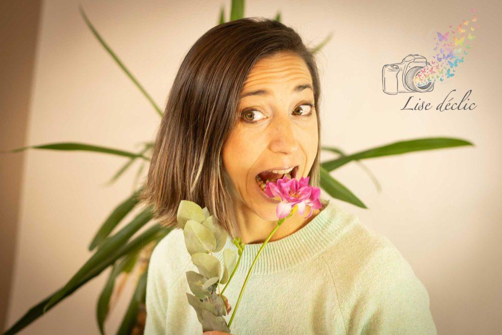 Portrait en studio d’une femme souriante tenant une fleur rose entre les dents – séance photo confiance en soi Lise Déclic