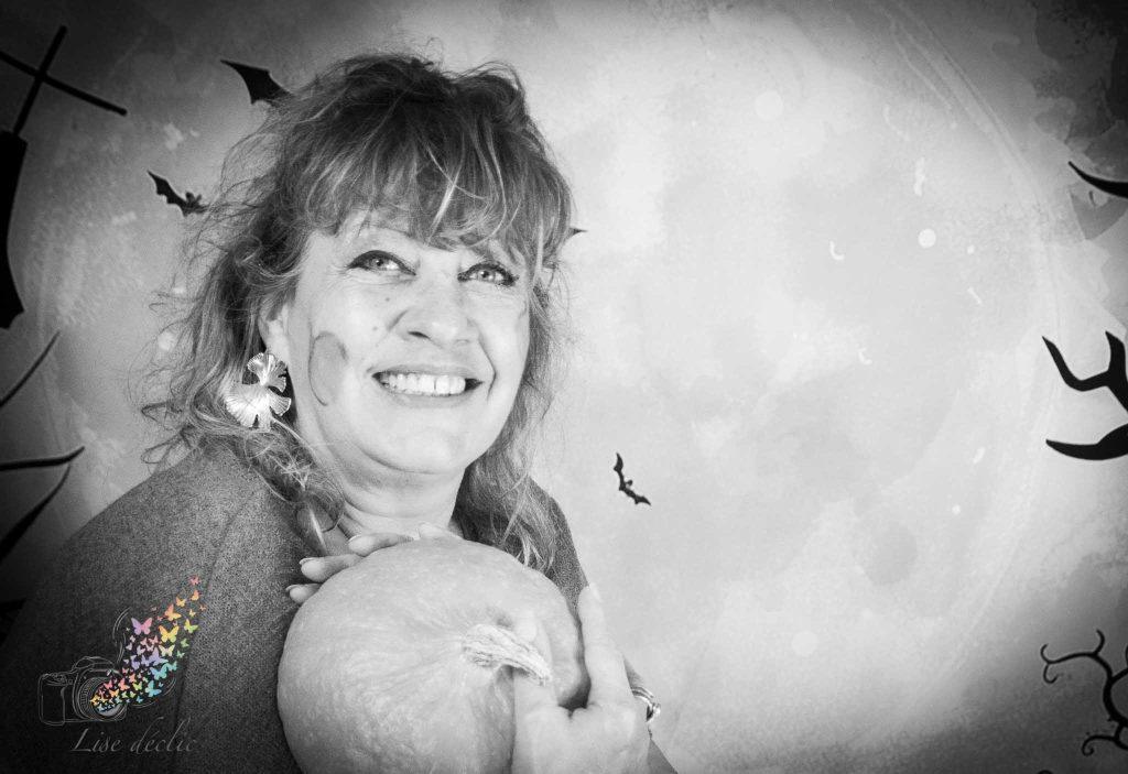 Femme souriante tenant une citrouille lors d’une mini séance photo Halloween en noir et blanc
