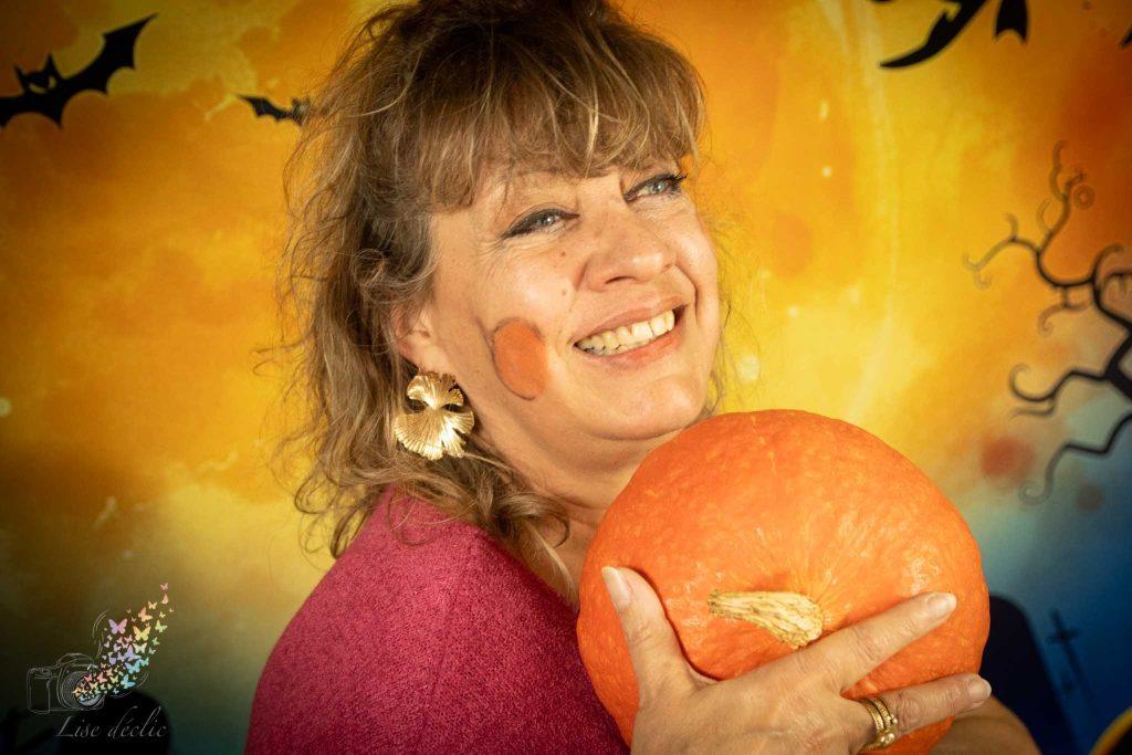 Femme souriante tenant une citrouille lors d’une mini séance photo Halloween