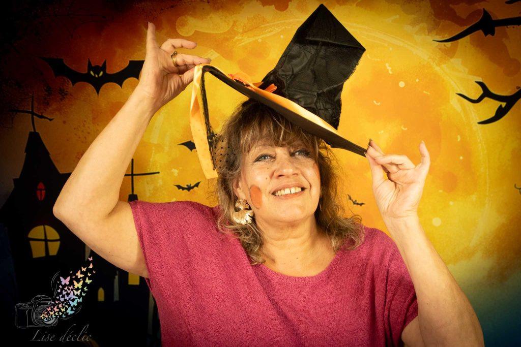 Femme souriante portant un chapeau de sorcière lors d’une mini séance photo Halloween