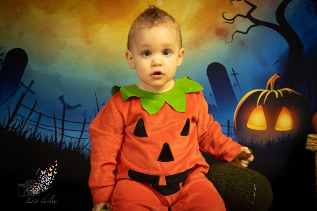 Bébé en costume citrouille assis devant décor Halloween avec citrouille lumineuse