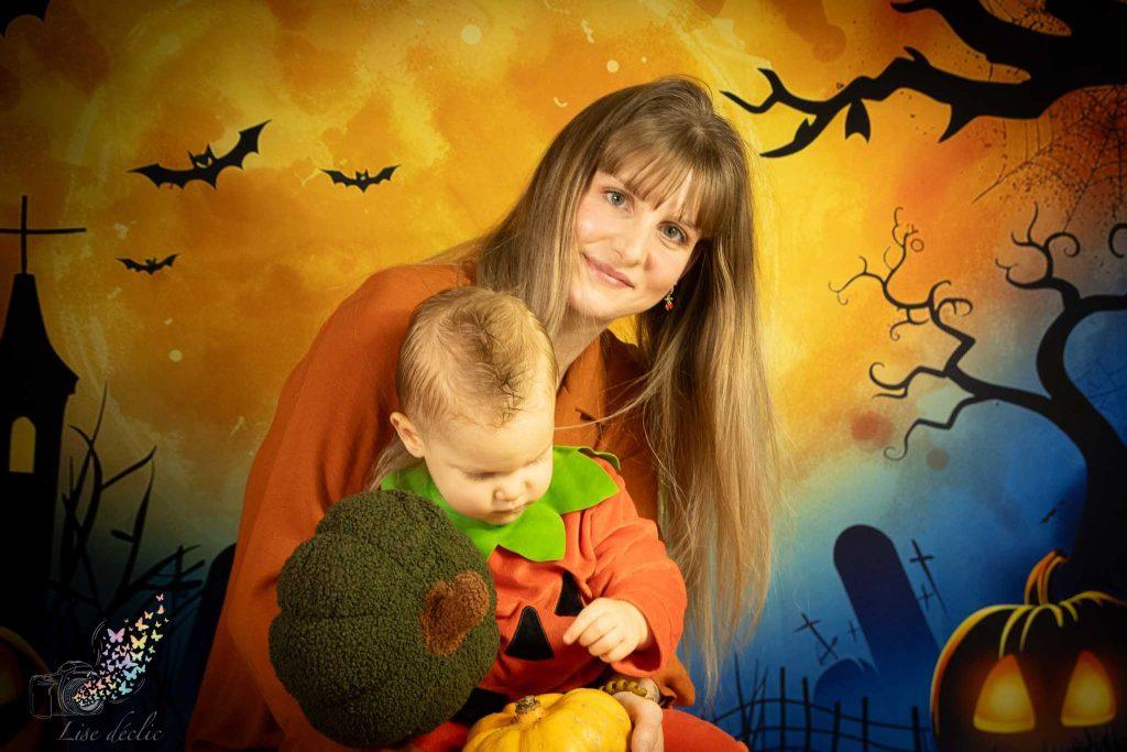 Maman avec son bébé déguisé en citrouille devant décor Halloween coloré