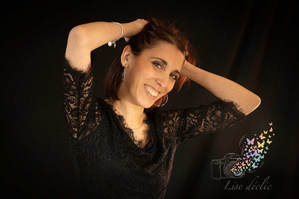 Portrait d’une femme souriante bras relevés, fond noir – séance photo S’aimer soi-même Lise Déclic